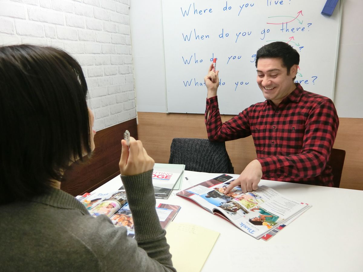 高田馬場校のレッスン風景。講師がホワイトボードの前で笑いながら教材を指している